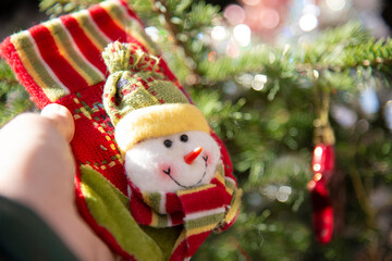 Boot for gifts with a snowman in a child's hand on the background of a Christmas tree.