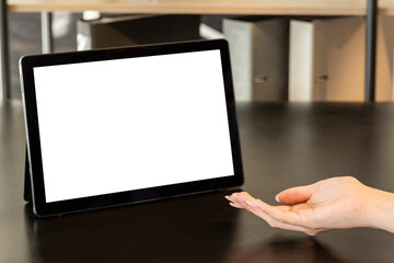 Online conference. Distance work. Presenting gesture. Sales manager. Female hand with open palm tablet computer blank screen on wooden table workplace interior copy space.