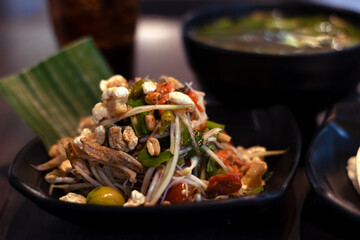 Thai papaya in a black plate with a green underneath and a blurred fish bowl as a background.