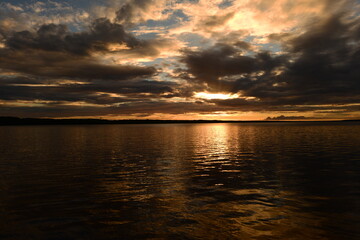 Fototapeta premium Glowing sunlight on the cloudy twilight sky is reflected by colorful light and shadows on the lake water