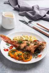 Baked sea bass with tomato pepper lemon and herbs in a ceramic plate on a gray concrete background. Perch fish cooked in the oven. Copy space