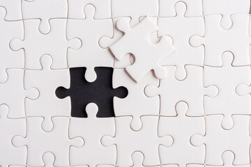 Top view flat lay of paper plain white jigsaw puzzle game texture incomplete or missing piece, studio shot on a black background, quiz calculation concept