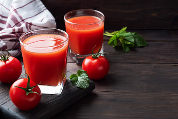 Tomato juice in glass glasses and fresh ripe tomatoes on a branch. Dark wooden background with copy space.