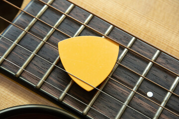 Yellow guitar pick on acoustic guitar