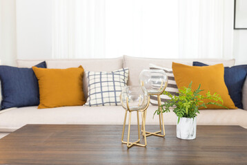 Blue and yellow pillows on a white sofa with glass vase and plant pot on table, living room interior.