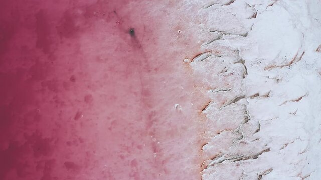 Aerial over a pink salt lake showing the contrast between the crystalized salt and the pink waters.