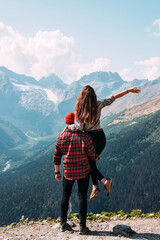 Naklejka premium Beautiful couple among the mountains. A couple in love in the mountains, back view. The man lifted the woman into his arms. The couple travels among the mountains. Hiking in the mountains. Copy space