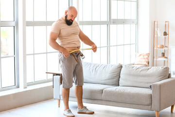 Overweight man measuring his waist at home. Weight loss concept