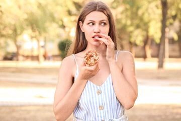 Beautiful young woman with sweet donut outdoors
