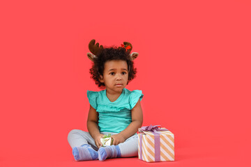 Cute African-American baby girl with Christmas gifts on color background