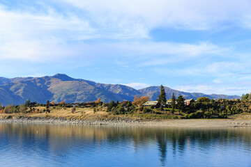 Fototapeta na wymiar Peaceful autumn landscape with solitary holiday boat on the calm waters with beautiful mountain background at Lake Hawea, New Zealand.