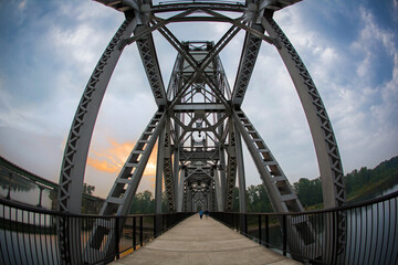 A fisheye, upward view of a walking bridge at dusk, with blue sky and clouds
