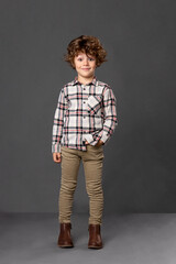 Frontal portrait of a curly little boy in casual clothes. Happiness kid concept, freedom, isolated on a grey background.