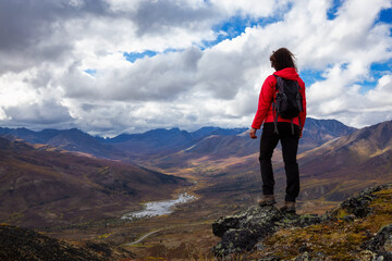 Obraz premium Woman Standing and Looking at Scenic Road and Mountain Range on a Cloudy Fall Day in Canadian Nature. Taken in Tombstone Territorial Park, Yukon, Canada.