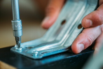 Shallow focus images of man assembling furniture at home using a  screwdriver.