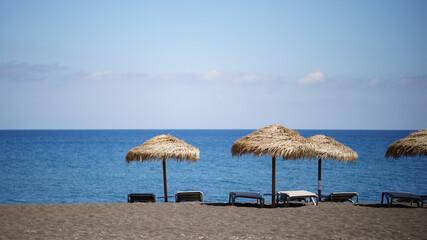 Perissa beach covered with black sand view with sunbeds and umbrellas on Santorini, Greece.