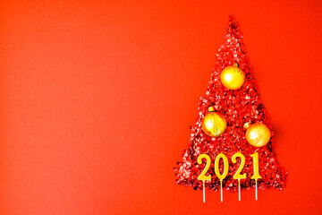 Christmas tree made by shiny confetti on red background. 2021 year gold candles. New Year and Merry...