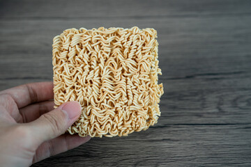 Hand holding instant noodle on wooden background.