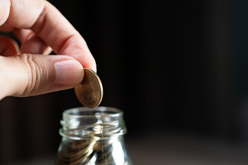 Hand putting coins in glass jar, saving  money concept.