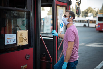 Man with medical protective mask and gloves entering the bus on a public transportation station.