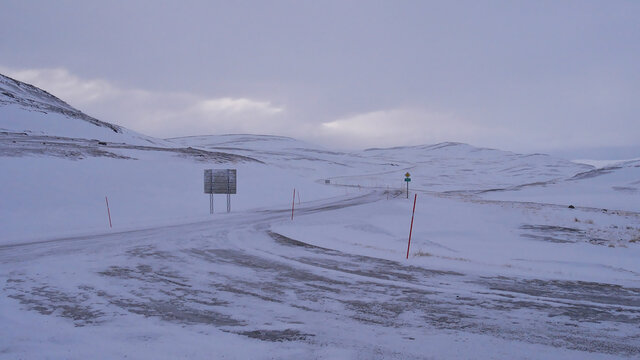 Road junction of European route E69 in Skarsv&aring;g near popular Nordkapp, Norway, Scandinavia in winter time with red colored snowplow markings, road signs and snow-covered landscape in winter time.