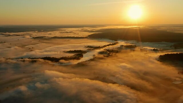 Aerial view of sunrise with fog above river Desna, Ukraine. Drone flies backwards above beautiful morning landscape with a fog while golden sunrise. Huge water evaporation over the lake in the summer.
