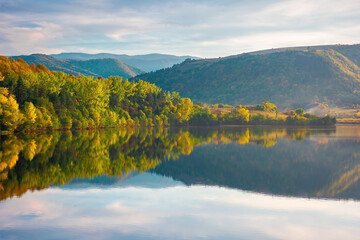 gilau lake of cluj country in evening light. beautiful landscape of romania in autumn. reflection on the calm water surface. trees in colorful foliage. sunny weather