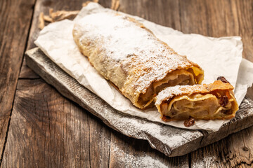 Homemade pear strudel, decorated with cinnamon, raisins powdered sugar on a rustic background. Food recipe background