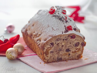 Christmas cake cut off. Pound cake decorated with red ribbons, sugar powder and dried cranberries upon white background. Selective focus.