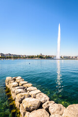 The city and bay of Geneva, Switzerland, with its emblematic 140 meter-high water jet fountain on the Lake Geneva, seen from a stone jetty by a sunny summer morning.