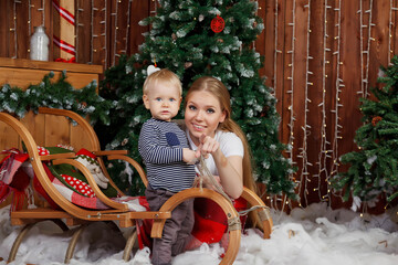 Pretty young woman with one-year-old child playing by Happy New Year tree. Mom with cute son in Merry Christmas decorated room. They are smiling and happy. Concept of family holiday. Copy space