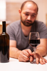 Man having alcohol addiction holding a glass of red wine. Unhappy person disease and anxiety feeling exhausted with having alcoholism problems.