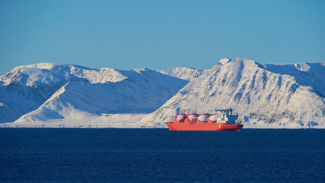 Big red painted LNG (liquefied natural gas) carrier vessel lying at anchor in the arctic ocean in front of S&oslash;r&oslash;ya island with snow-covered mountains near Hammerfest, Norway, Scandinavia in winter.