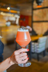 Close up of woman hand holding glass of draft lager beer. Fruit beer in a glass. Eating out in restaurant concept.