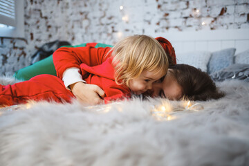 Mom with daughter in red warm sweaters on the bed. Happy motherhood. Warm family relationships....