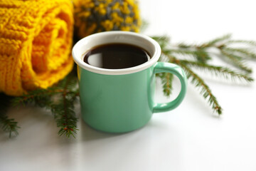Greenery ceramic cup with black coffee on the knitted yellow scarf and fir branches background closeup. Sweet home winter mood concept