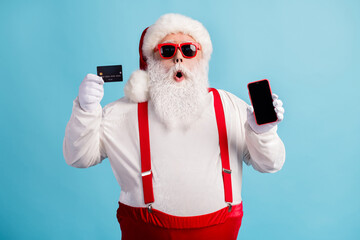 Fototapeta na wymiar Portrait of his he attractive amazed white-haired Santa holding in hand demonstrating credit card gadget order shop buy good product cash back isolated bright vivid shine vibrant blue color background