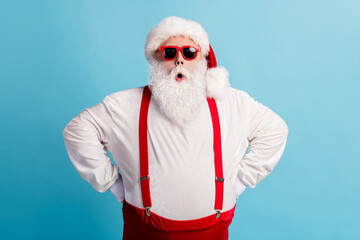 Fototapeta na wymiar Photo of pensioner old man grey beard hands hips self-assured shock late wake up present delivery wear santa costume red suspenders spectacles white headwear isolated blue color background