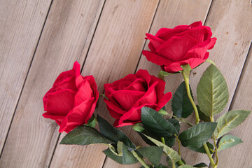 Three red roses on wood grain background