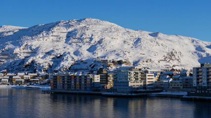 Front view of residential buildings located at the shore in Hammerfest, Norway, Scandinavia at the arctic sea with snow-covered mountains equipped with avalanche protection in winter time.