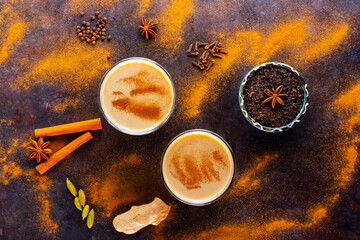 Masala chai tea on a black background. Two transparent glasses of masala tea and scattered various spices. Top view