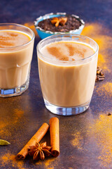 Masala chai tea on a black background. Two transparent glasses of masala tea and scattered various spices. Top view