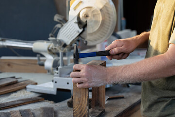 Carpenter man with hammer hitting nails on wood and on construction background