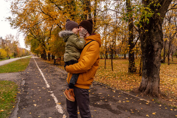 Father have a fun with his little son in a park. Autumn colors, green, orange. Son kiss dad on the alley.