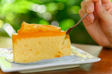 Piece of orange cake with fresh orange slice on top and spoon on white dish