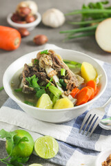 Sop Tulang Sapi or Indonesian clear  beef soup mixed with some vegetables such as carrot, potato, cabbage, and green bean. Served on ceramic bowl , with sambal and onion crackers as condiments.