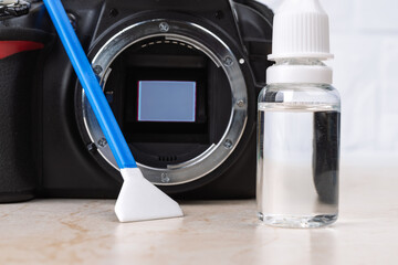Dslr camera with raised mirror, liquid sensor cleaner and swab on a table. Routine cleaning of dust...