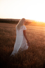 Fototapeta na wymiar A young blonde girl stands in a field and looks at the sunset. Village life, slow living 