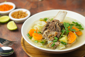 Sop Tulang Sapi or Indonesian clear  beef soup mixed with some vegetables such as carrot, potato, cabbage, and green bean. Served on ceramic bowl , with sambal and onion crackers as condiments.