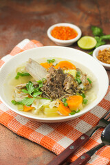 Sop Tulang Sapi or Indonesian clear  beef soup mixed with some vegetables such as carrot, potato, cabbage, and green bean. Served on ceramic bowl , with sambal and onion crackers as condiments.